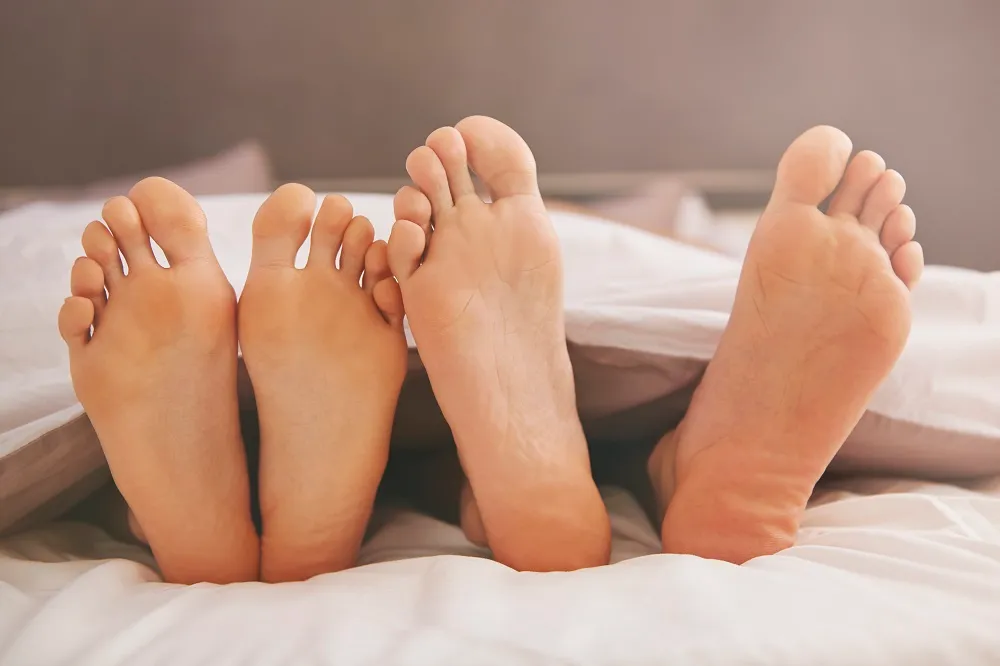 A group of feet sticking out from under covers, showing various stages of recovery after bunion surgery.